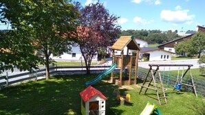 Un parque infantil con un tobogán, columpios y una casita.