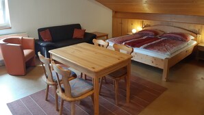 Una habitación acogedora con techo de madera, cama con ropa de cama estampada, sofá negro, mesa de madera con sillas y un radiador.