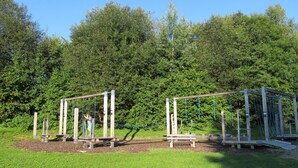Un parque infantil con columpios y una estructura para escalar en un área con césped.