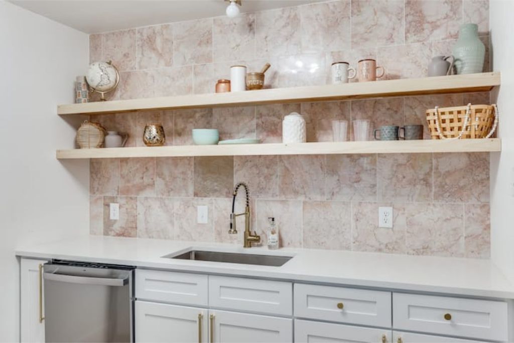 A kitchen with marble backsplash, white cabinetry, and a built-in dishwasher.