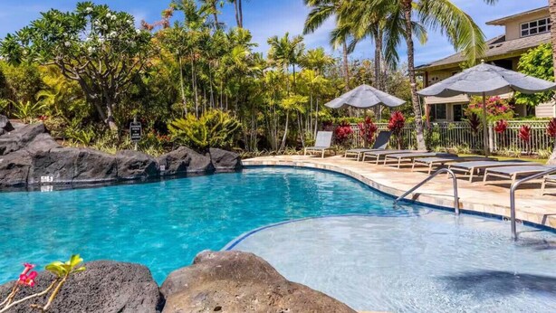 Piscina cristalina rodeada por vegetação tropical e um edifício com alpendre coberto.