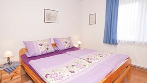 Une chambre à coucher avec un lit en bois, une literie violette et deux lampes fixées au mur.