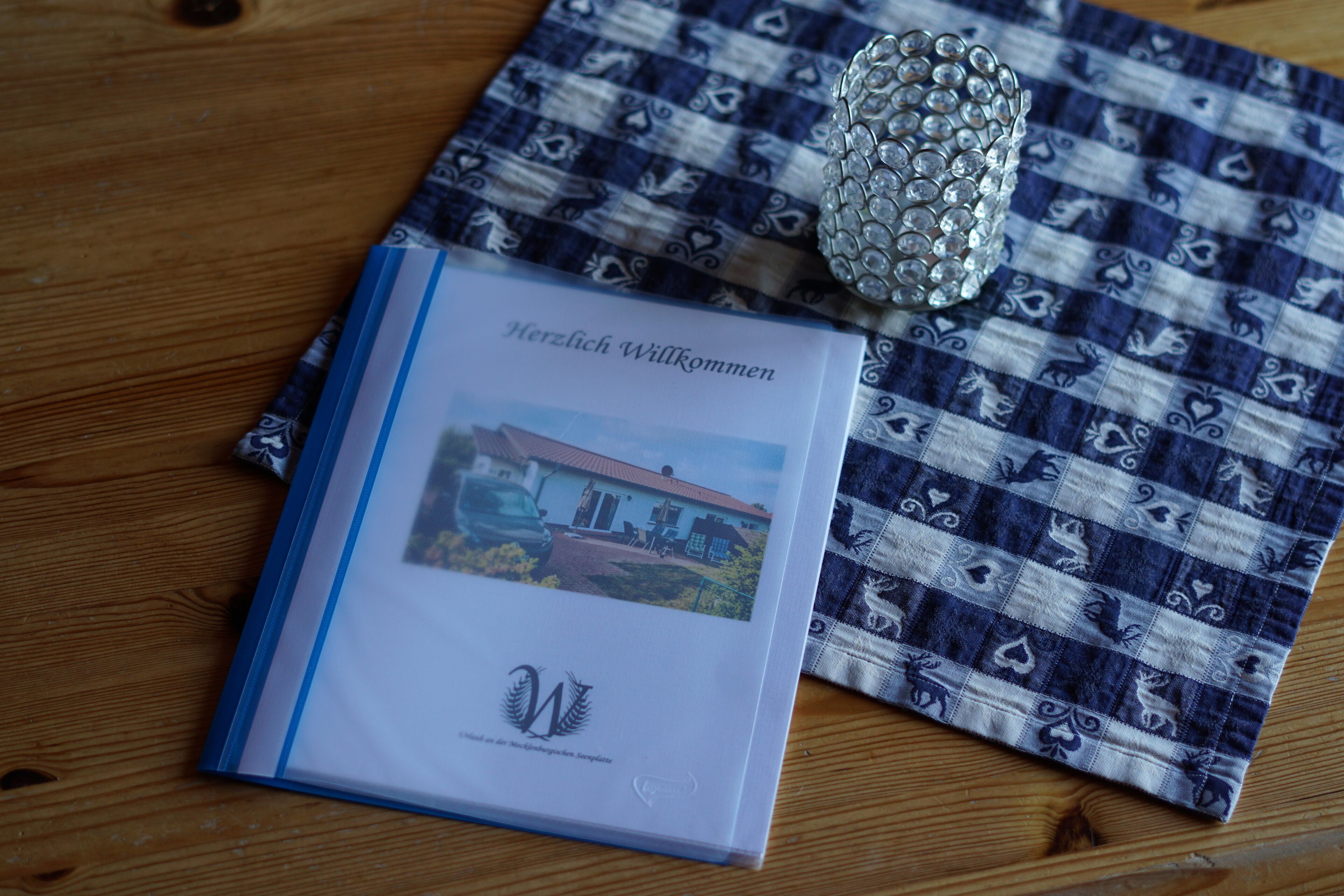 Ein Buch mit dem Titel „Herzlich Willkommen“ auf einem Holztisch mit blau-weiß kariertem Tuch.