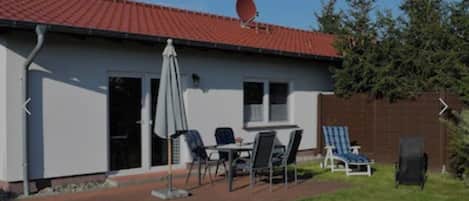 A single-story building with a red-tiled roof, a satellite dish, and a patio area with outdoor furniture.
