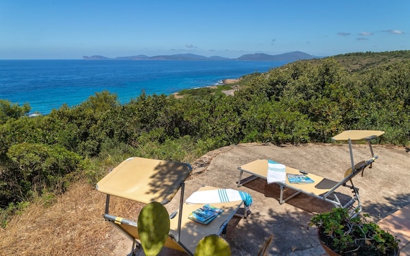 Una terraza frente a la playa con dos tumbonas, una mesa y una planta en maceta.