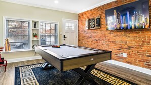 A pool table in a room with a brick wall and a cityscape painting.