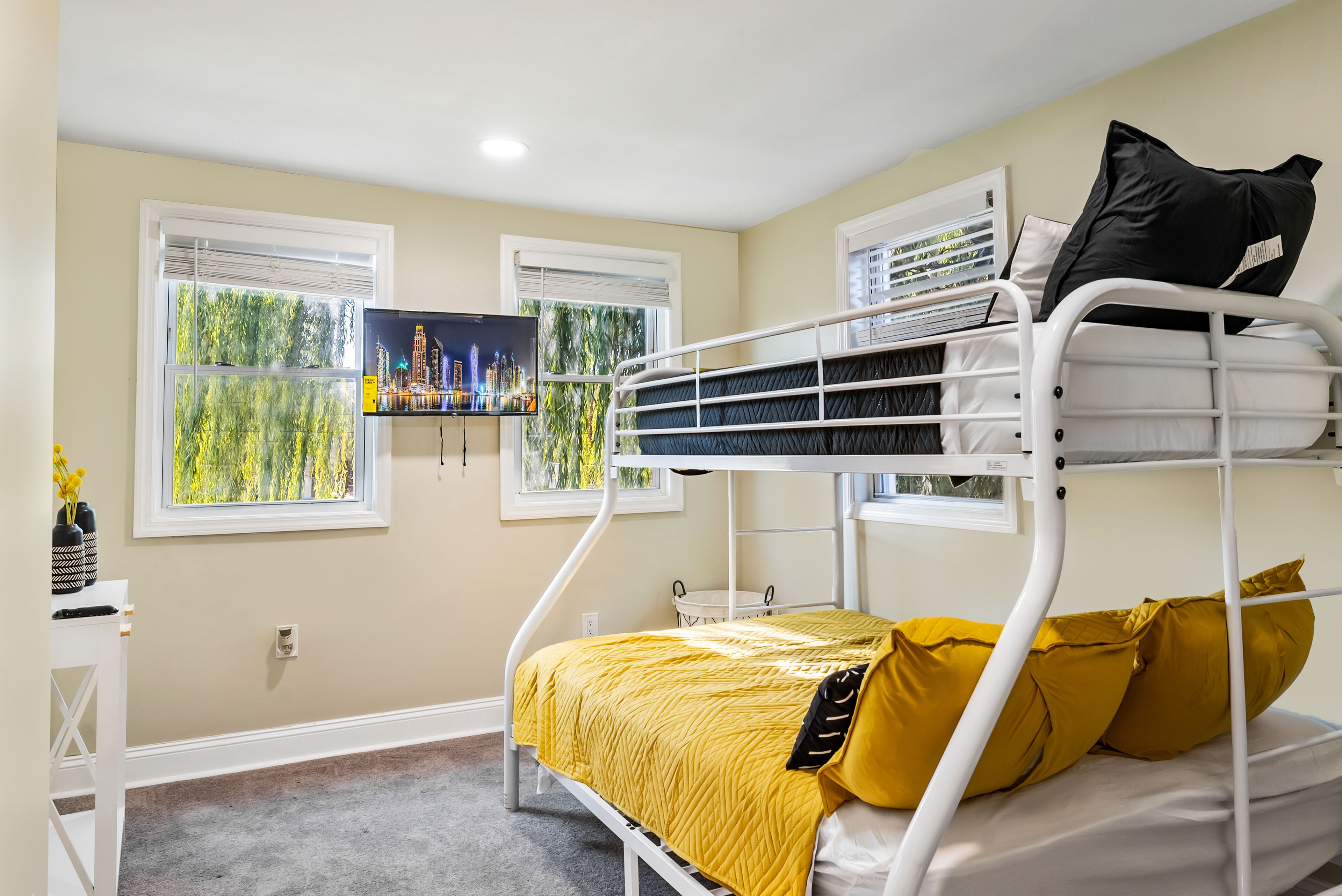 A bunk bed room with a cityscape view, a desk, and a window with blinds.
