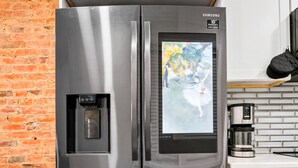 A stainless steel refrigerator with a water dispenser and a built-in ice maker, placed in a kitchen with white cabinets and a brick wall.