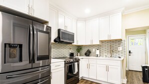 A modern kitchen with stainless steel appliances, white cabinetry, and a wooden floor.