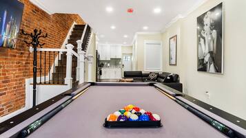 A pool table with balls, a staircase, a kitchen, and a living area with a couch and artwork.