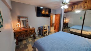 Ein Schlafzimmer mit einem Bett, einem Schminktisch mit Spiegel, einem Fernseher und einem Deckenventilator.