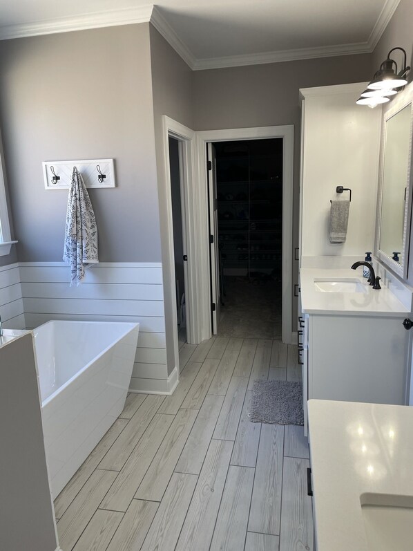 A modern bathroom with a bathtub, vanity, and a walk-in closet.