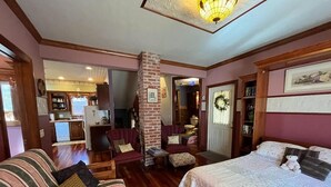 A cozy room with a bed, a sofa, and a fireplace. There is a brick pillar and a door leading to another room. - Four Winds - 1st Floor (Saint Ansgar)