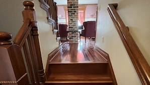 A wooden staircase with a stone pillar in the center, leading to a room with a fireplace and two chairs. - Four Winds - 1st Floor (Saint Ansgar)