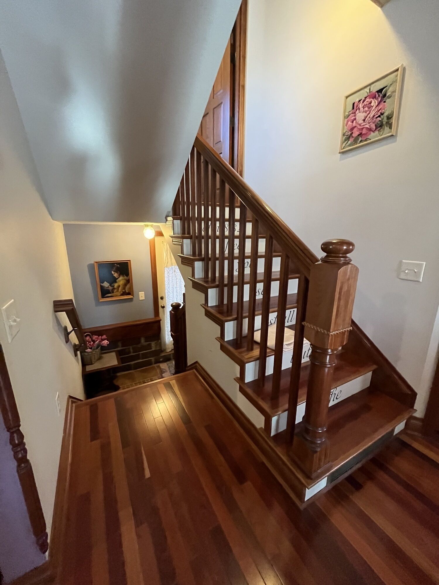 A wooden staircase with a handrail, a painting on the wall, and a light fixture above the door.