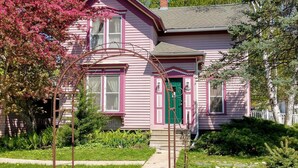 A pink house with a green door, surrounded by a well-maintained garden and a metal archway.