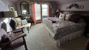 A bedroom with a large bed, a nightstand, a chair, a dresser, and a window with curtains.
