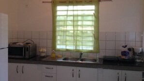 Una cucina con mobili bianchi, un forno a microonde, un lavello e una finestra con tenda verde.