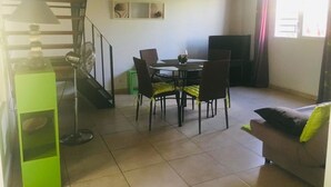 Un'area pranzo con tavolo e sedie, un armadietto verde, una ventola e una scala.