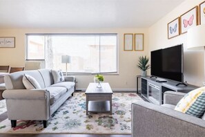A living room with a sofa, a coffee table, a TV, and a window with blinds.