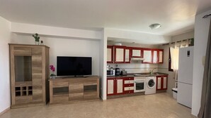 Una cocina compacta con televisor, un mueble de madera, lavadora y refrigerador.