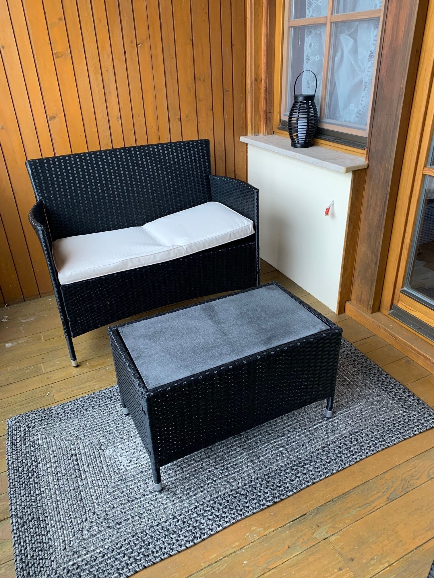 A black wicker sofa with a white cushion and a matching ottoman on a gray rug.