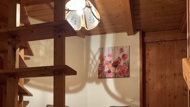 Un interior de madera con una lámpara de techo, dos sillas, un otoman redondo y una alfombra estampada.