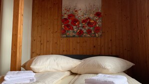Una cama bien hecha con sábanas y toallas blancas, una pared de madera y un cuadro con flores rojas.