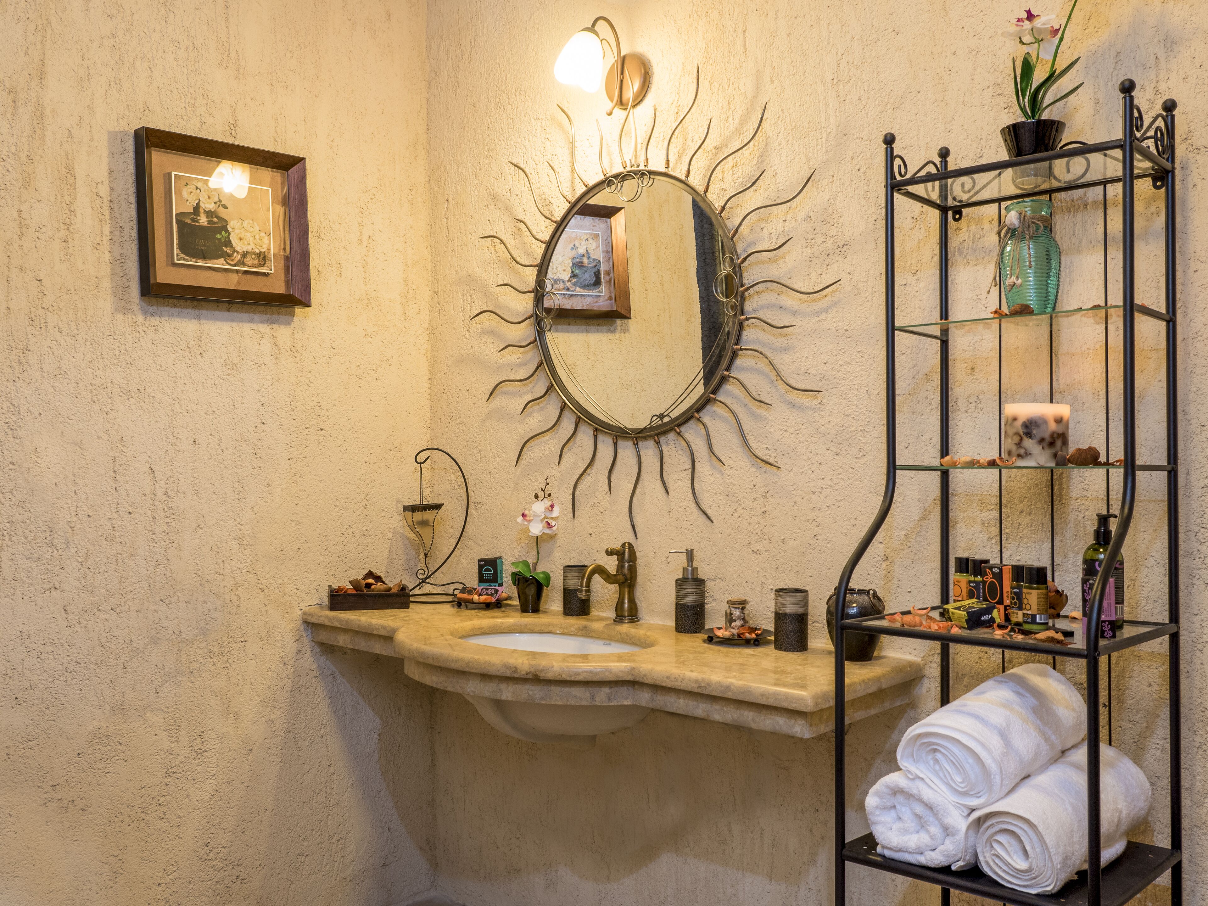 Een badkamer met een wastafel van steen, een spiegel met zonachtige decoratie, een handdoekhouder en toiletartikelen.