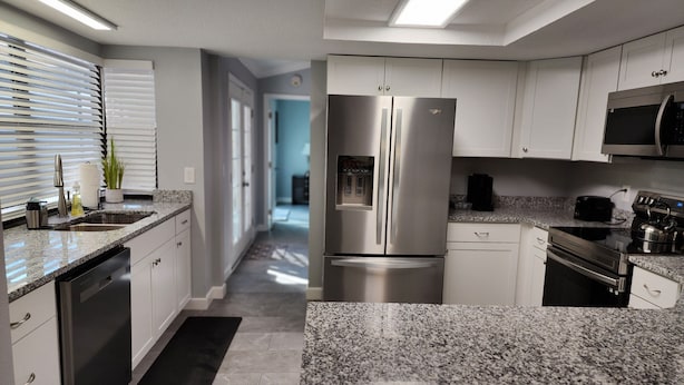 Una cocina moderna con electrodomésticos de acero inoxidable, armarios blancos y encimeras de granito.
