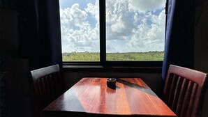 Ett träbord med två stolar, ett fönster med gardiner och en utsikt över en molnig himmel och ett grönt landskap.