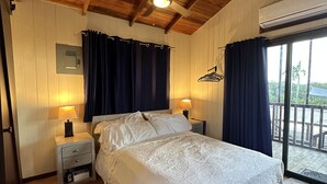 Ett sovrum med ett träpanelat tak, en säng med vita sängkläder, två sängbord med lampor och en utsikt genom en glasdörr ut mot ett utomhusområde.