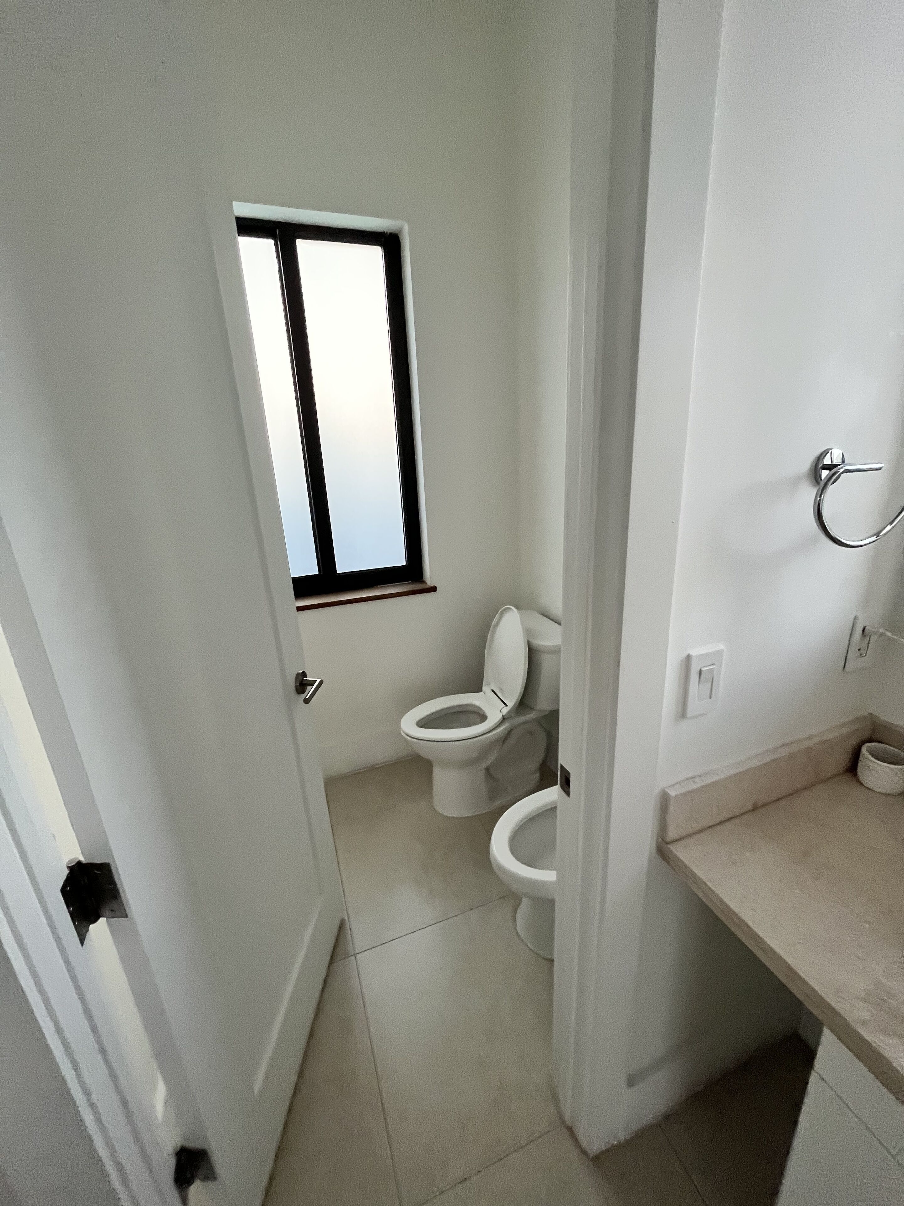 A small, compact bathroom with a toilet, a window, and a towel rack.