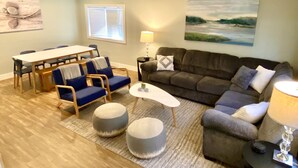 A living room with a dining table, chairs, a sofa, ottomans, and a lamp. - Newly remodeled LAKE HOUSE with HOT TUB, Game Room, Large DECK on PAW PAW LAKE (Coloma)