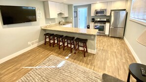 A modern kitchen with a central island, bar stools, stainless steel appliances, and a flat-screen TV. - Newly remodeled LAKE HOUSE with HOT TUB, Game Room, Large DECK on PAW PAW LAKE (Coloma)
