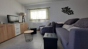 Un salon moderne avec un canapé, un téléviseur, une lampe et une fenêtre avec des rideaux.