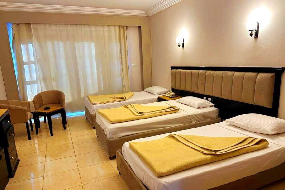 A hotel room with two single beds, a desk, a chair, and a large window with curtains.