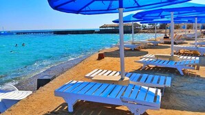 Une plage avec une eau d’un bleu limpide, des chaises longues et des parasols.