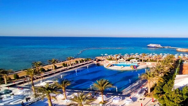 Un complexe hôtelier doté d’une grande piscine, de palmiers et offrant une vue sur la mer.