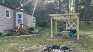 A backyard with a wooden pergola, a fire pit, a grill, and a house with a porch. - Cozy Nothwoods home next to ATV/Snowmobile trails (Laona)
