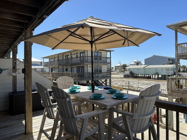 Una terraza de madera con una mesa y sillas, un paraguas y vistas a edificios y una playa al fondo.