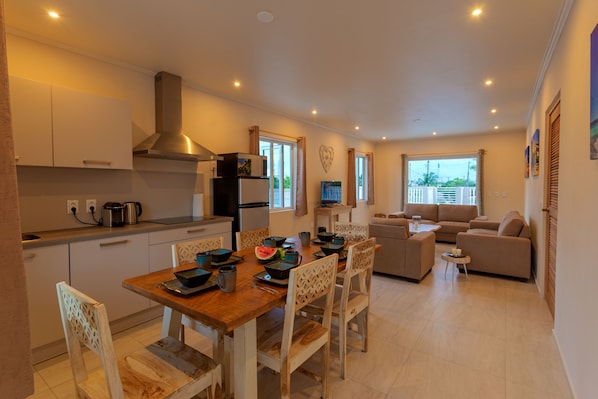 Une cuisine moderne avec des meubles blancs, une table à manger en bois et un coin salon comprenant un canapé et des fauteuils.