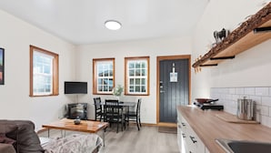 A compact living space with a kitchenette, a dining area, and a seating area with a fireplace. - Steps from the Beach! ~ Near Wild Pacific Trail! ⎮ Orca (Ucluelet)