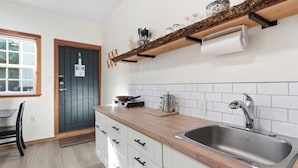 A modern kitchen with a wooden countertop, stainless steel sink, and a black door. - Steps from the Beach! ~ Near Wild Pacific Trail! ⎮ Orca (Ucluelet)