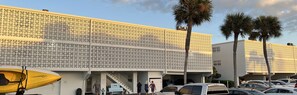 Un edificio moderno con fachada estampada, zona de estacionamiento techada y palmeras.