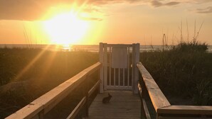Une promenade en bois menant à une plage, avec un coucher de soleil en arrière-plan.