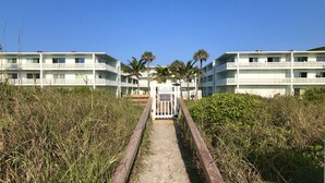 Un chemin mène à un bâtiment blanc doté de nombreux balcons, avec des palmiers en arrière-plan.