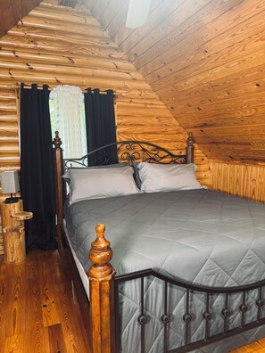 Una cama individual con cabecera de madera y colcha gris acolchada en una habitación con paredes de madera y techo inclinado.