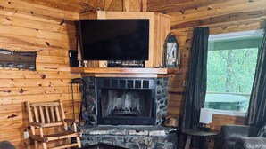 L’intérieur d’un chalet confortable, avec des murs en bois, une cheminée en pierre, un canapé en cuir et un téléviseur fixé au-dessus de la cheminée.