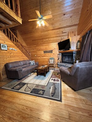 Interior de una cabaña de madera con un sofá, una mesa de centro, una chimenea y un televisor.